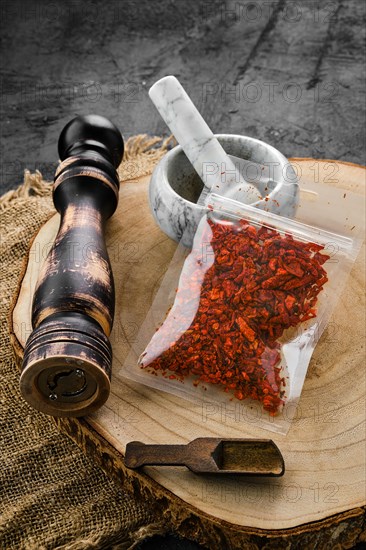 Wooden cross section with crushed paprika in plastic package and stone mortar and mill