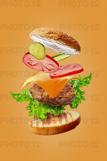 Burger with flying ingredients isolated on orange background