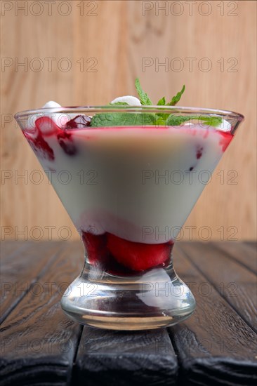 A glass of youghurt with marshmallow and raspberries decorated with mint leaves
