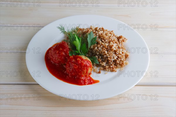 Traditional russian meatballs with buckwheat and tomato sauce on wooden table