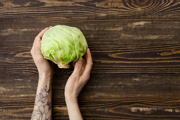 Overhead view of fresh iceberg lettuce in hands over wooden background