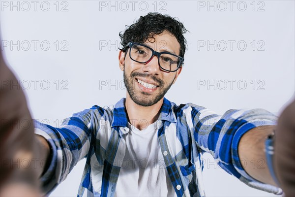 Handsome man taking a selfie looking at the camera on isolated background. Teenage guy taking a self portrait isolated. Guy with beard and glasses taking a self portrait isolated