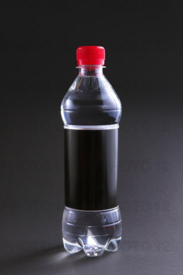 Plastic bottle of water with black label and red cap on table