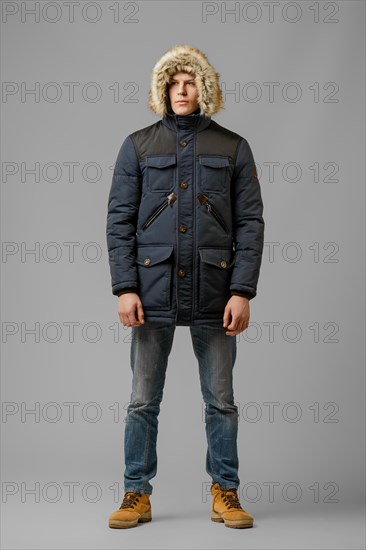 Full length portrait of handsome man in warm coat with hood posing in studio
