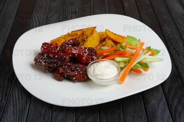 Buffalo chicken wings with fried potato and carrot and celery sticks on a plate