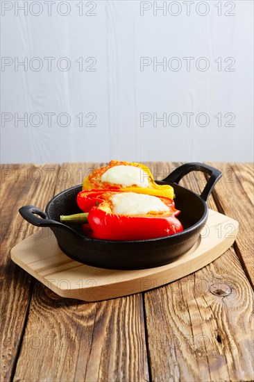 Bell pepper stuffed with meat with melted cheese mozzarella on top baked in oven in cast iron skillet. Top view. Natural wooden background