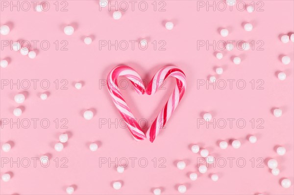 Small striped Christmas candy cane sweets forming heart on pink background