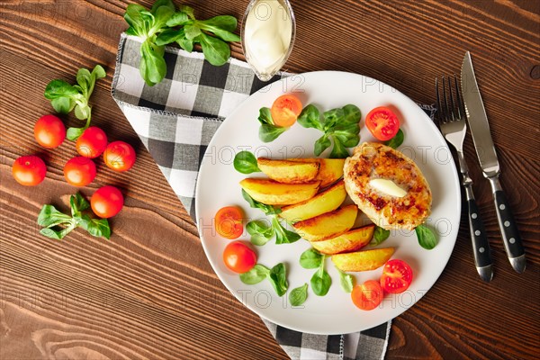 Fried chicken cutlet with potato slices served with tomato cherry and corn salad. Traditional belorussian food