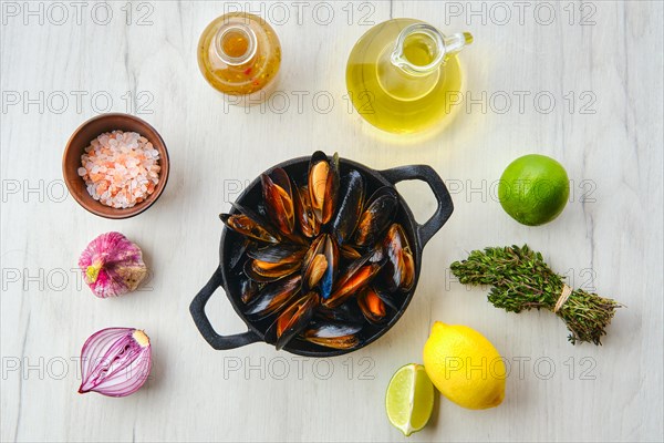 Top view of unpeeled mussels in cast iron skillet with spice and herbs