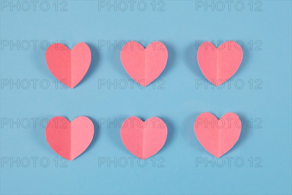 Cute pink paper craft hearts arranged in two rows on pastel blue background