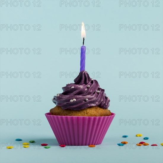 Purple burning candles decorative muffins with colorful star sprinkles against blue backdrop