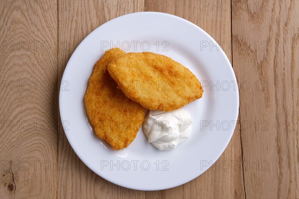 Top view of potato cutlet in breading stuffed with ham served with sour cream on wooden table