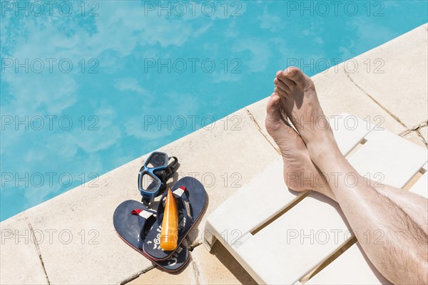 Legs near goggles with lotion flip flops near pool