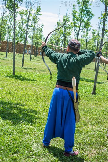 Archer with bow in traditional clothes shooting an arrow