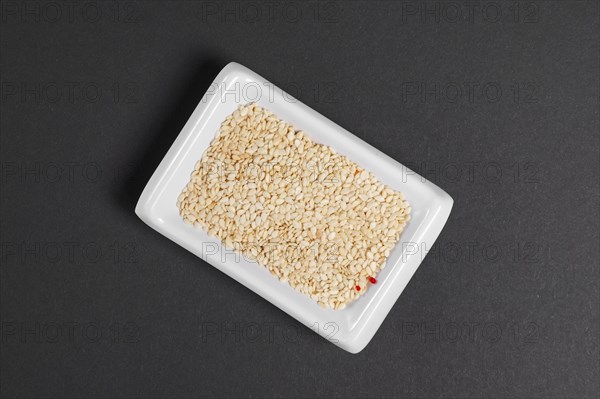 Top view of white sesame seeds in a little dish on gray paper