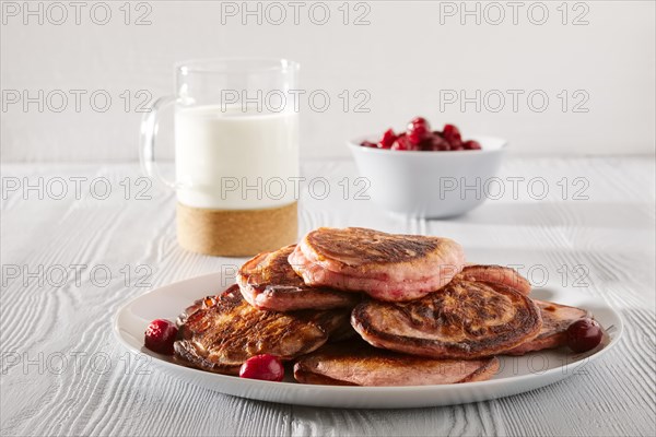 Pancakes with cherry and glass of milk on white kitchen table