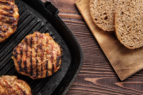 Top view of cast iron grill pan with beef cutlets and freshly baked brown bread