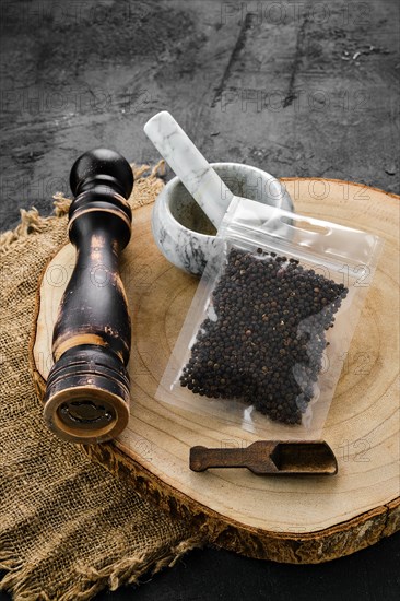 Wooden cross section with peppercorn in plastic package and stone mortar and mill