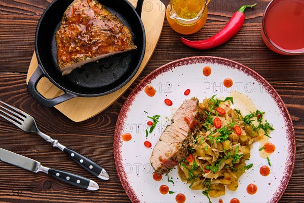 Top view of oven-baked meat with braised cabbage and zucchini and hot spicy sauce