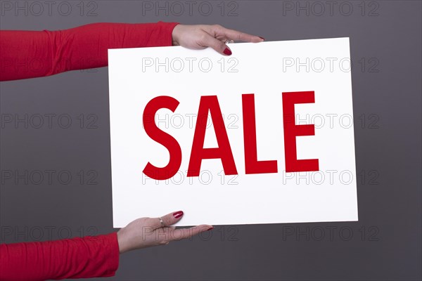 Female hands holding a Sale poster. Studio shot