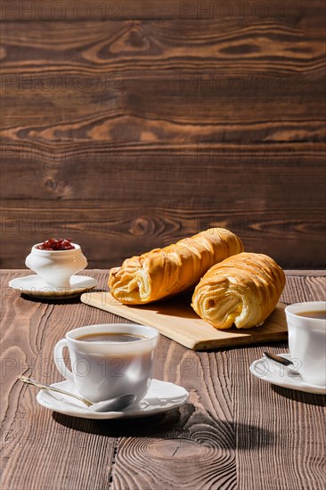 Rolled buns and coffee on wooden table in morning sunlight. Photo with shallow depth of field