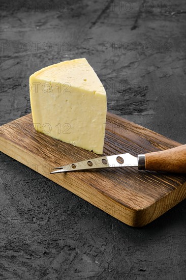 Triangular piece of hard cheese on wooden cutting board