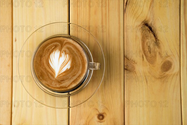 Overhead view of cappuccino in transparent glass cup on wooden table