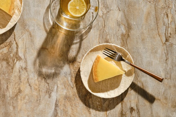 Top view of piece of lemon tart with tea under direct sunlight with hard shadows on the table