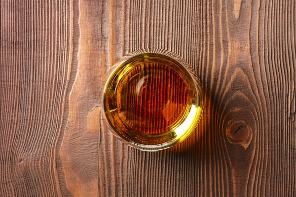 Top view of snifter glass with pure whiskey on dark wooden table