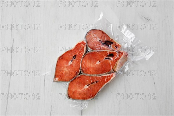 Overhead view of raw salmon steak in vacuum packaging on light background