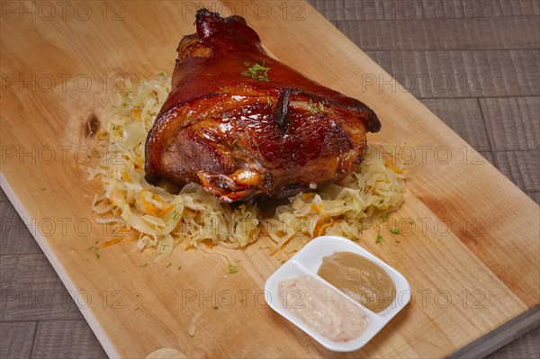 Top view of knuckle with sauerkraut served with mustard and horseradish on wooden cutting board