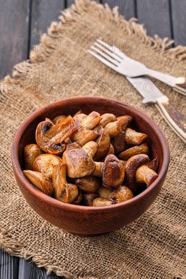 Clay plate with roasted mushrooms on dark wooden table