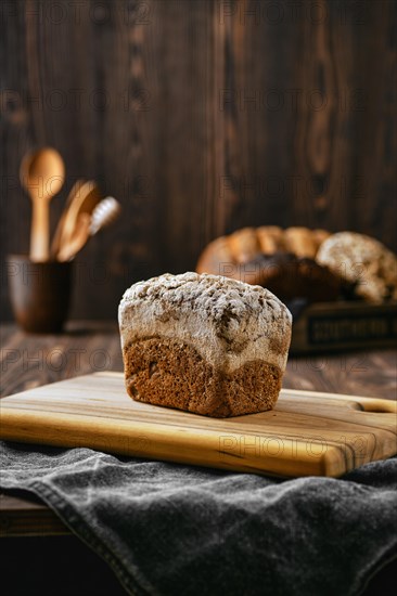 Loaf of artisan rye bread with flour topping on wooden cutting board