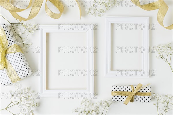 Golden ribbon gift boxes baby s breath flowers near wooden frame white backdrop