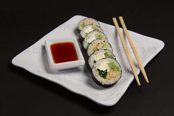 Angle view of portion of chicken teriyaki rolls served on black paper with soy sauce and hashi