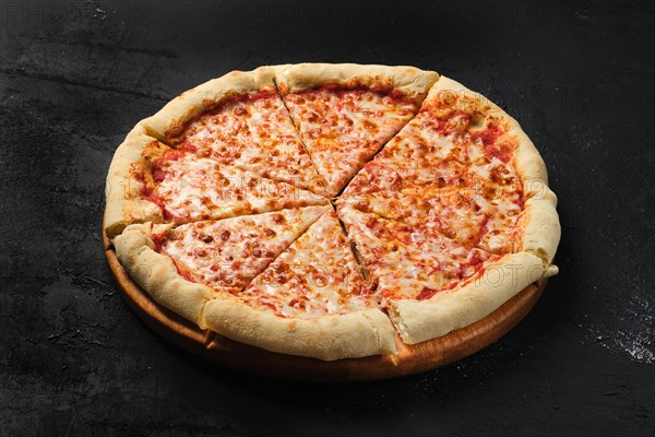 Cheese pizza cut in slices om dark background