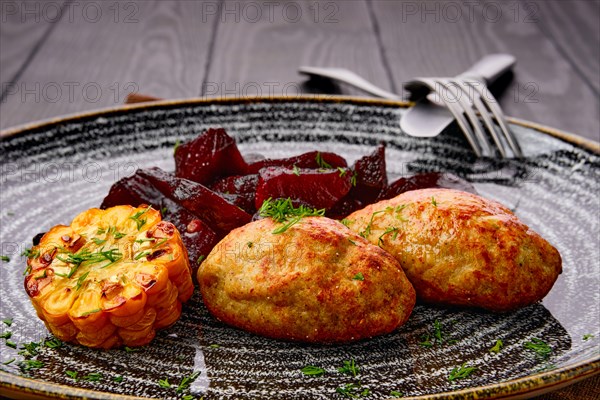 Close up view of fried pork cutlet with roasted beetroot slices and grilled maize on dark wooden table