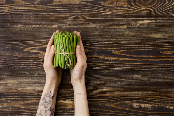 Overhead view of fresh green beans in hand over wooden background