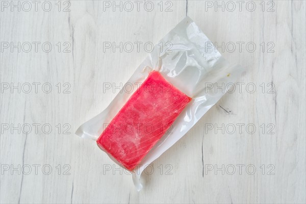 Raw frozen tuna fillet in vacuum packaging on wooden background