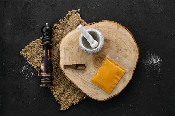 Wooden cross section with turmeric in plastic package and stone mortar and mill