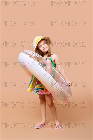 Cute child in sundress and straw hat with swimming ring playing in studio