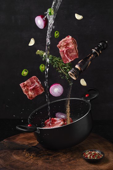 Chopped beef bones falling into saucepan with ingredients for bouillon stock