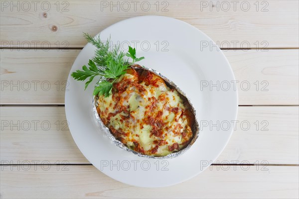 Top view of meat baked in foil with vegetables and cheese on wooden table