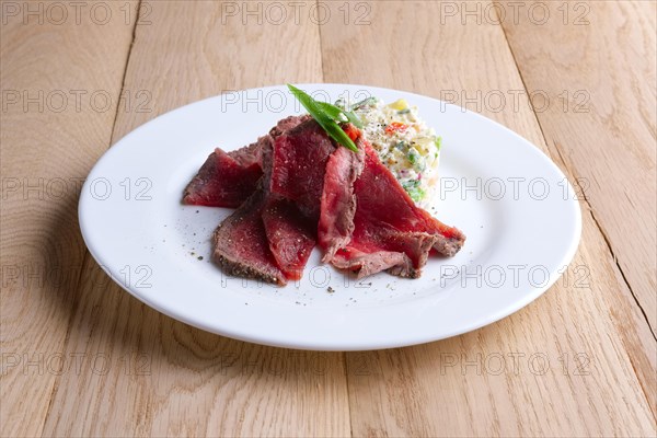 Roasted meat with salad olivier on wooden table