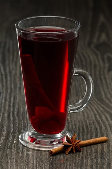 Glass of hot cherry tea with cinnamon on wooden table on dark wooden table