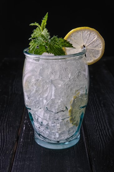 Cold cocktail with vodka and tonic in skull cup on dark wooden background