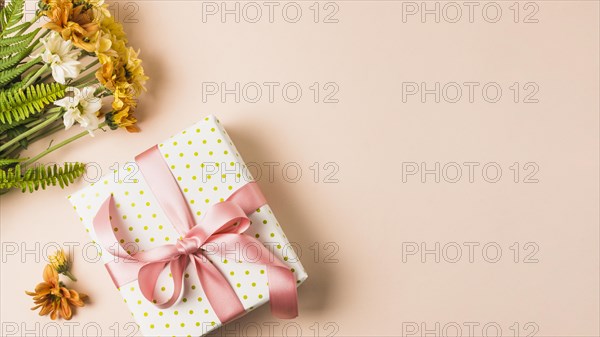 White yellow flower bouquet near wrapped present box peach surface. Resolution and high quality beautiful photo