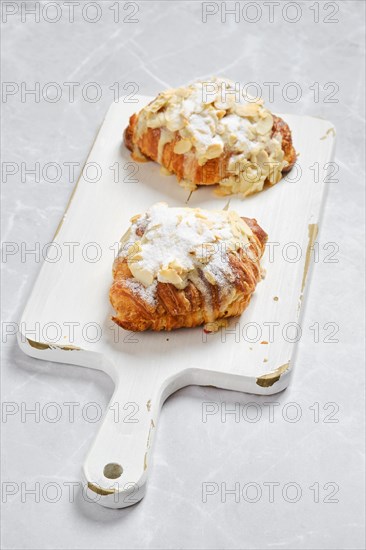 Two crispy croissants with caramel and peanut shavings on white serving board on marble surface