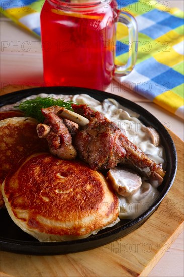 Fried in oven ribs with fritters and onion sauce. Cast iron pan on wooden cutting board and glass with cranberry juice