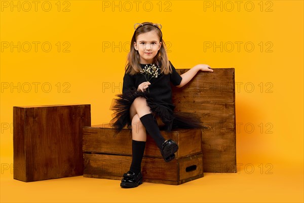 Young girl sitting among wooden apple boxes on orange background